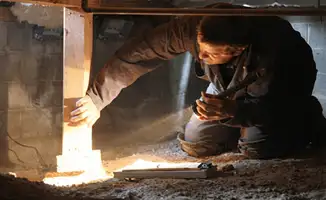 A professional inspecting wooden beams under the floor of a structure in New Orleans, LA